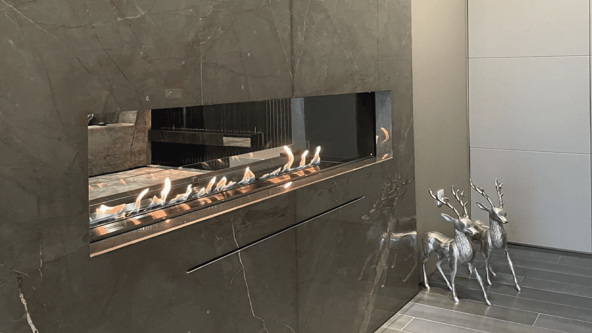 GlammBox EVOPlus bioethanol fireplace integrated in a luxury marble-clad living room with metallic deer sculptures.