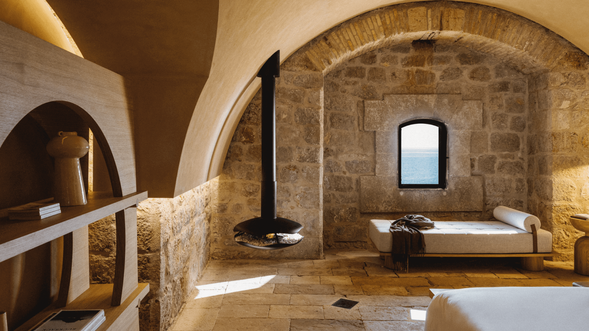 Perola suspended bioethanol fireplace by GlammFire in a rustic stone room with vaulted ceilings and sea view"