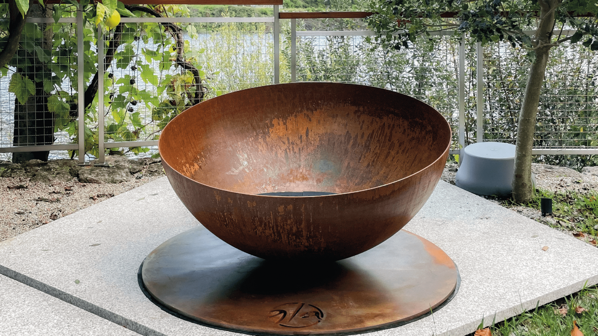 Solace fire pit by GlammFire in a rustic outdoor setting with a corten steel finish