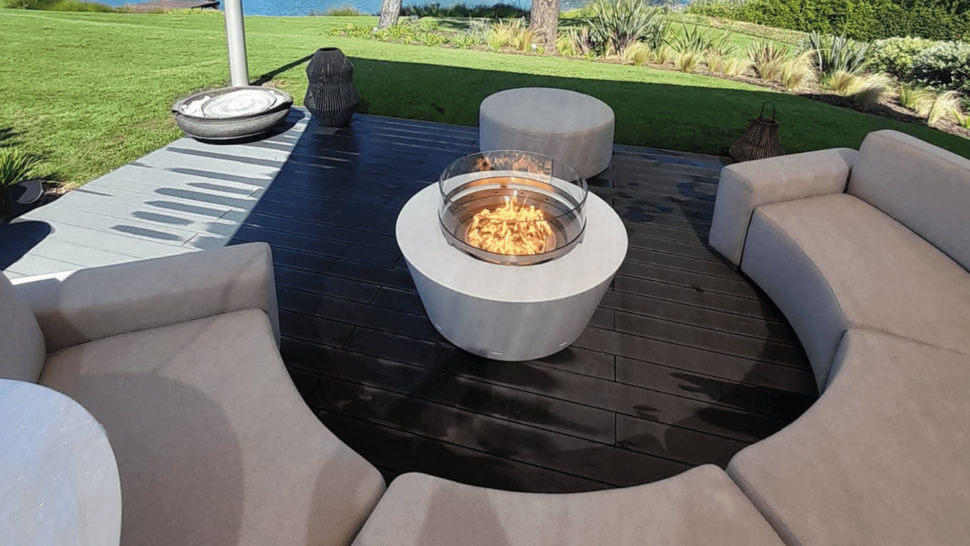 Gas fire pit in a modern outdoor seating area with a view of a lake and greenery